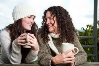 Teen daughter and mom each with a coffee mug, sitting and smiling at one another