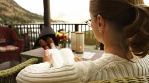 Christian woman practicing self-care by reading a book on a wooden porch