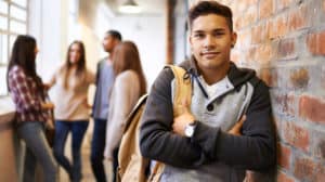 Teen leaning against a brick wall, lightly smiling