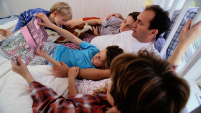 Three young kids hanging out on their parents’ bed with their mom and dad