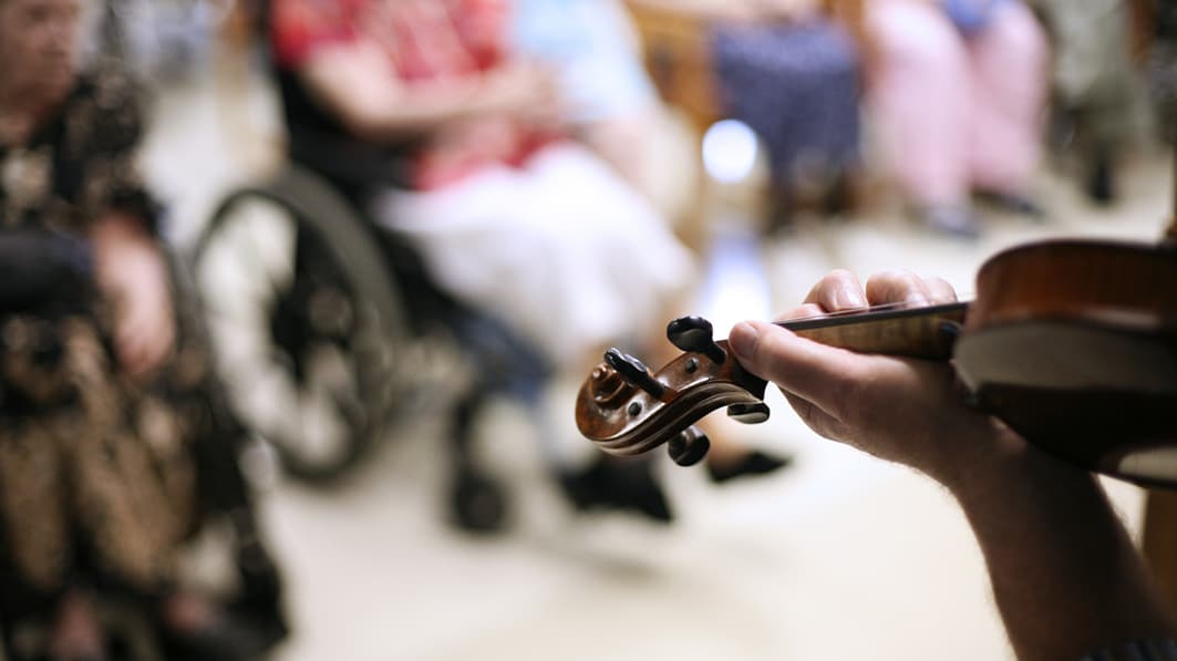 Hands play a violin at a nursing home where residents experience social isolation.