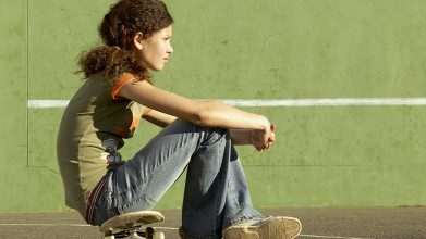 Profile view of teen girl sitting on skateboard and looking troubled