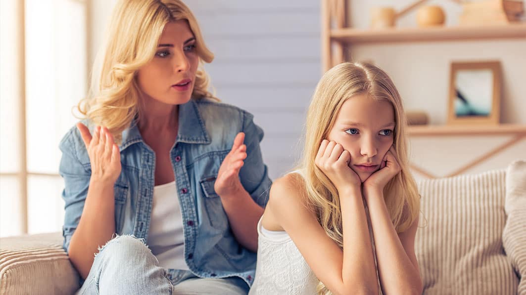 Frustrated mom trying to talk to her tween daughter who’s facing in opposite direction, looking indifferent
