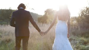 Bride and groom standing in a field holding hands