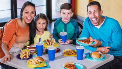 Mom, dad, and their two kids smiling around their fast food dinner table