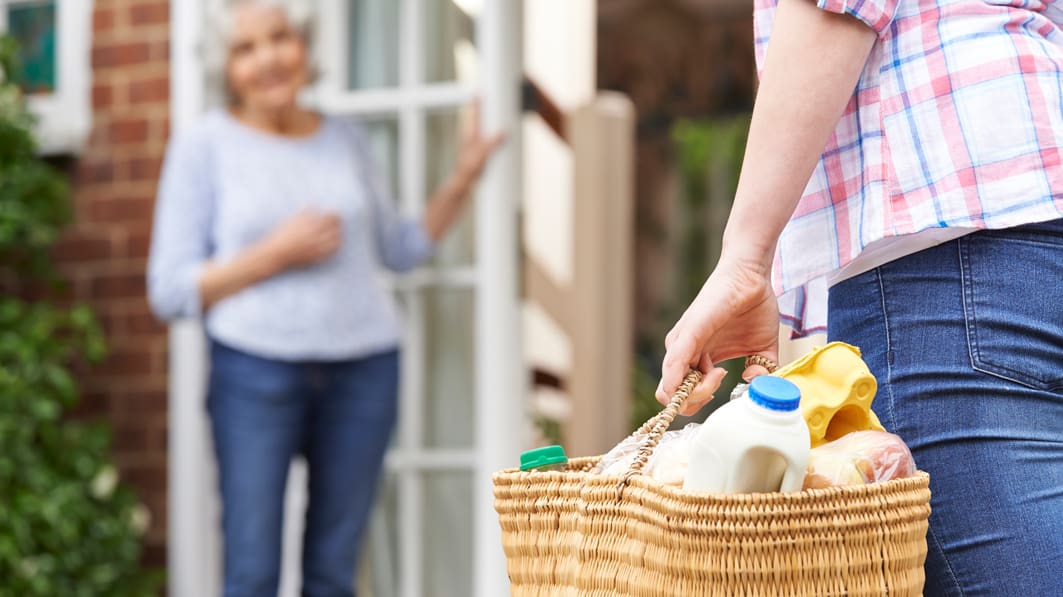 A caregiver bringing a basket of groceries to an elderly woman