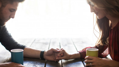 Couple sitting at a table holding hands and praying