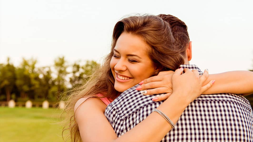 Happy, smiling, young wife tightly hugging her husband as they stand outside