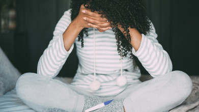 Woman sitting cross-legged, her head resting in her hands, as she appears distressed over a pregnancy test result