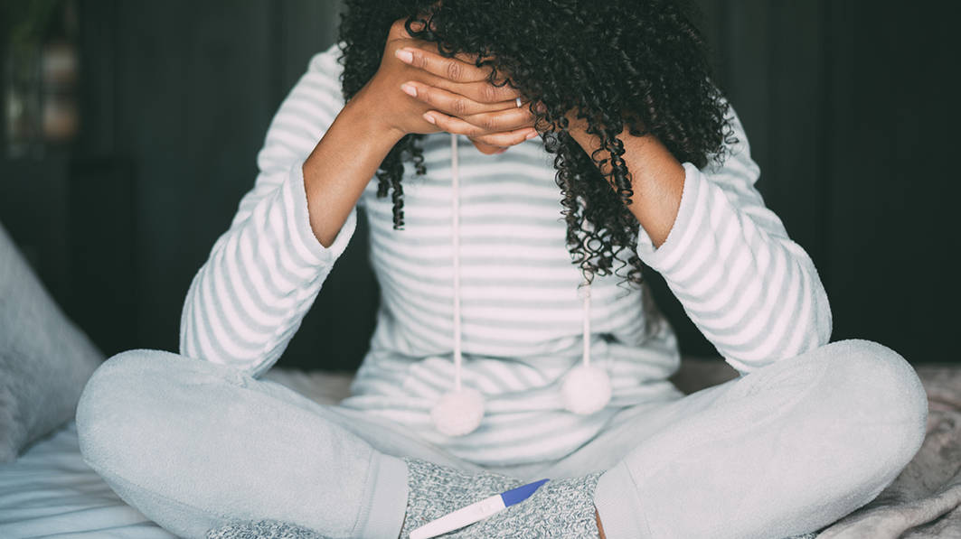 Woman sitting cross-legged, her head resting in her hands, as she appears distressed over a pregnancy test result