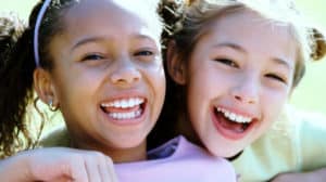Close up of faces of two young girls who are side hugging and laughing