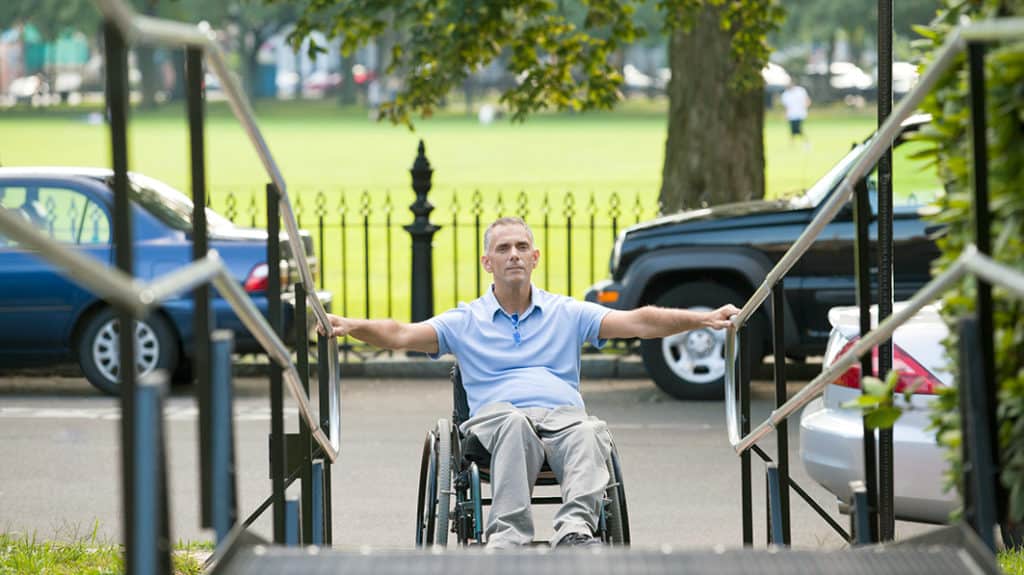 A disabled man in a wheel chair starting to go up a handicap ramp