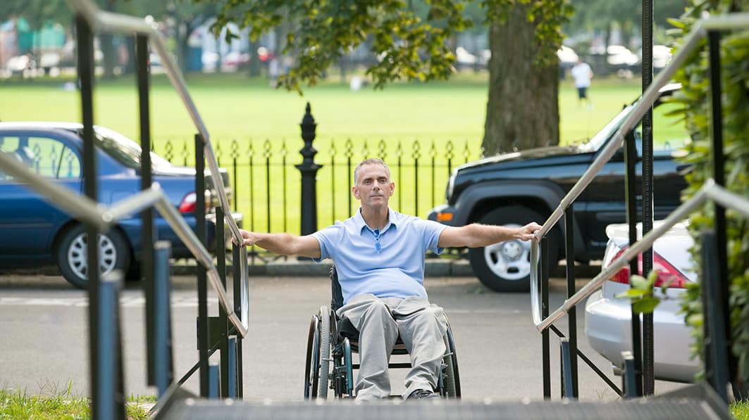 A disabled man in a wheel chair starting to go up a handicap ramp