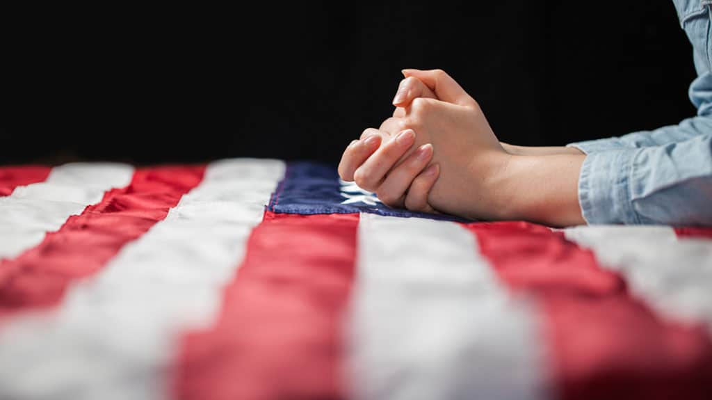 Hands praying over American flag