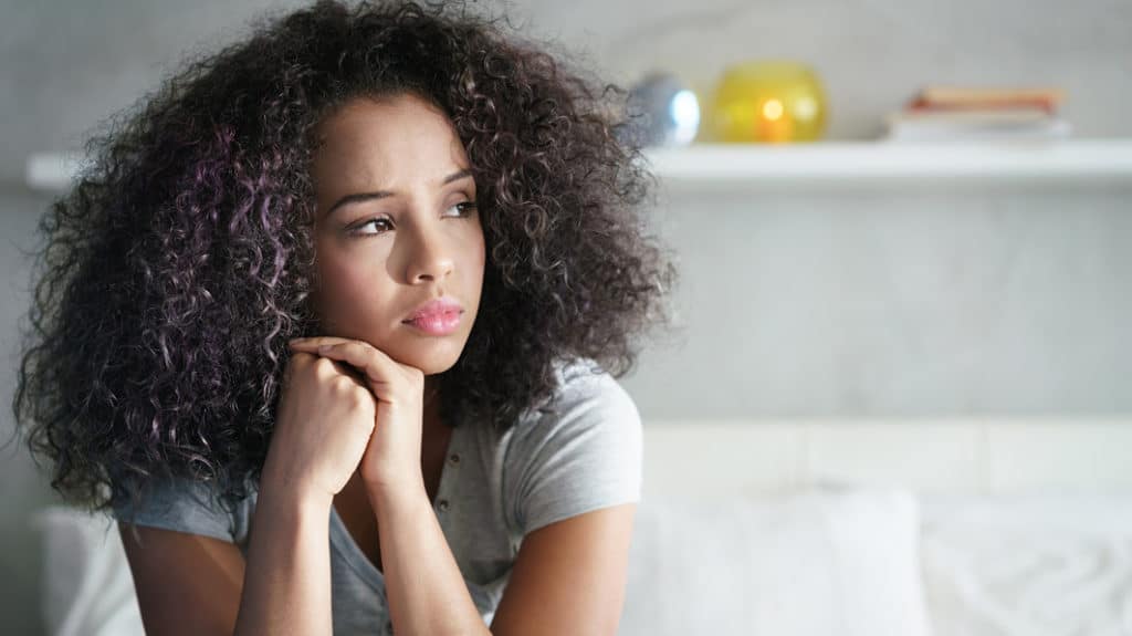 Serious teen girl looking away toward a window as she sits on her bed