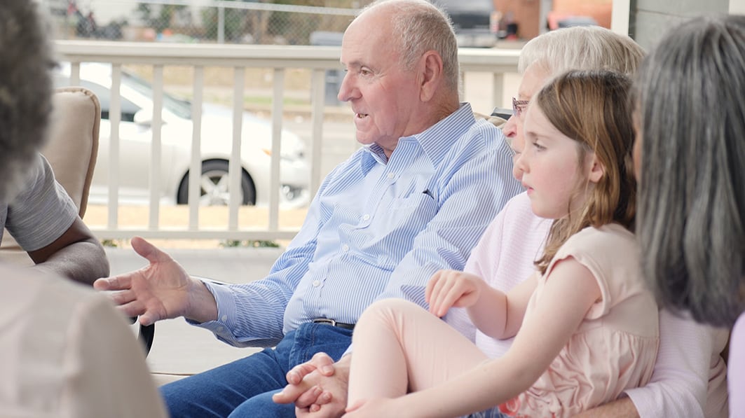 Grandparents sitting with their friends and grandchildren on the porch of their home