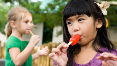 Two young girls eating popsicles outside