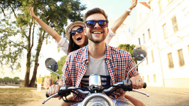 Happy young couple rides a motor bike down a street