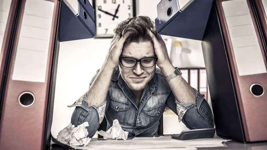 Man stressed surrounded by paper binders and crinkled paper