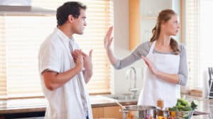 Young couple having argument in the kitchen. She's shunning him as he tries to explain himself.