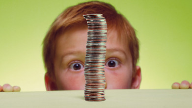 A boy peering over the edge of a table, looking wide-eyed at a big stack of quarters