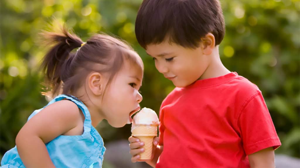 A young boy holding an ice cream cone, allowing a little girl to take a bite