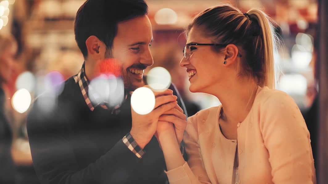 Laughing young couple leaning close to each other, holding hands while on a date in a restaurant