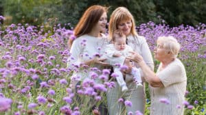Four generations of women - a grandmother, daughter, granddaughter and baby great granddaughter – standing in a flower field