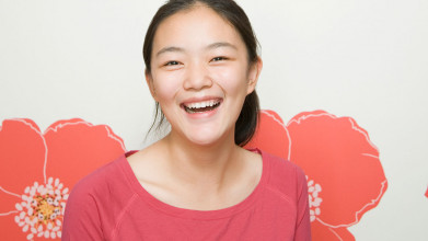 A smiling Asian teen girl against a white background with several large orange flowers