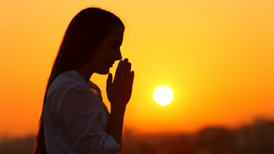 Silhouette of woman praying against backdrop of a sunset