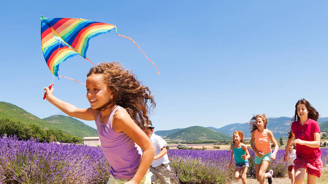Excited preteen girl running with rainbow kite through a lavender meadow