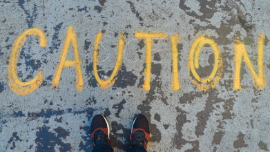 Shown from the perspective of someone looking down, the word ‘caution’ is spray-painted in large letters on the pavement