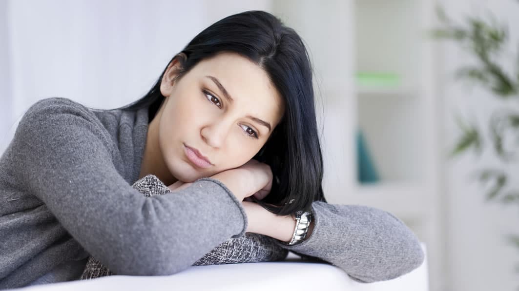 Contemplative young woman sitting at home, staring off into space while lost in thought