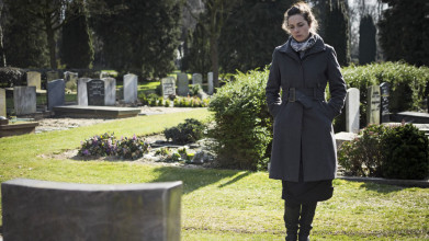 A sad woman standing in front of a headstone in a graveyard