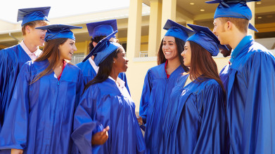 Group of smiling teens or young adults dressed in blue graduation gowns
