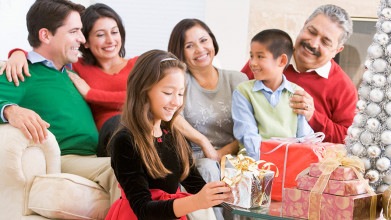 Joyful family of parents, two young kids, and grandparents, with the girl about to open a Christmas present