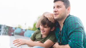 Dad has his arm affectionately wrapped around his smiling, young son’s head as they sit together outside