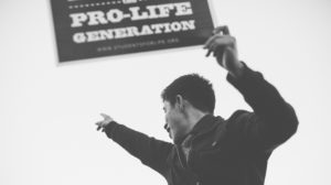 Black and white photo of young man holding up a pro-life sign and cheering at a rally