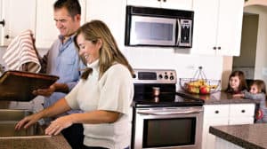 Happy couple washing dishes together while young kids watch