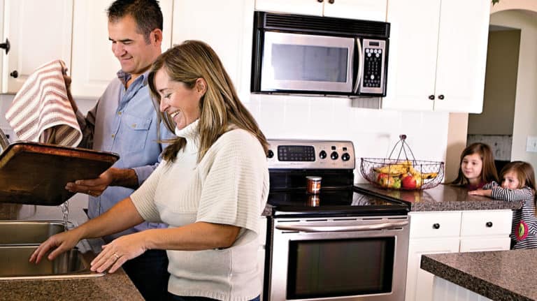 Happy couple washing dishes together while young kids watch