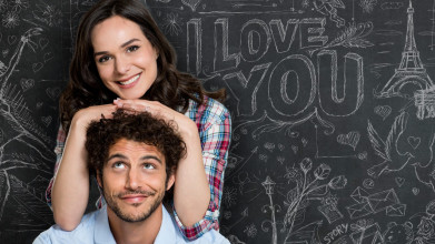 Smiling wife playfully resting her hands and chin on the head of her husband in front of a chalkboard that says “I love you”