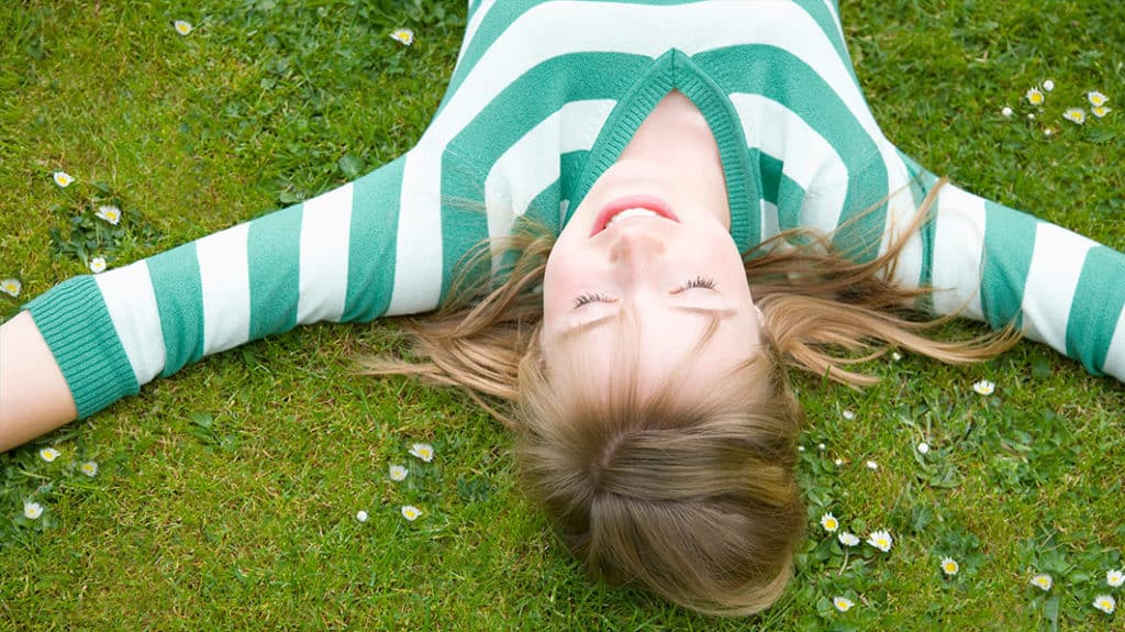 Peaceful, joyful-looking teen lying on grass with her arms stretched out
