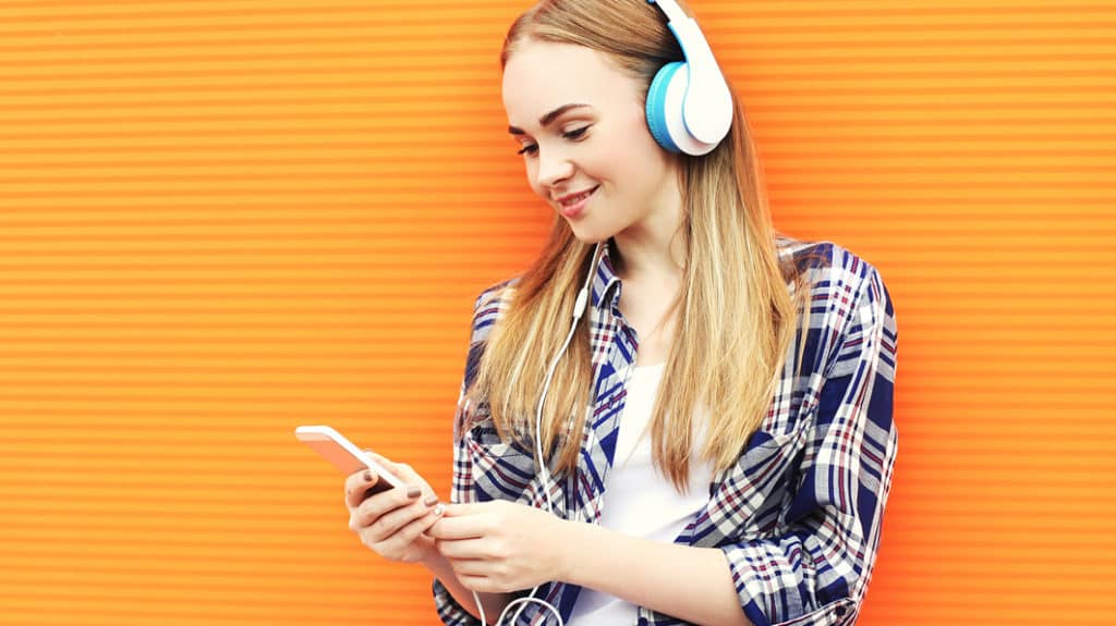 Smiling teen girl wearing headphones, listening to music and using a smartphone