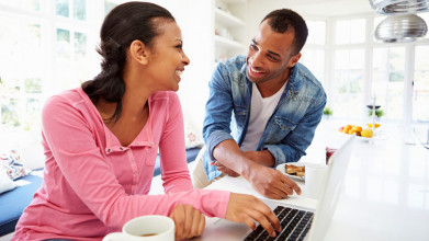 A man and a woman look smile at one another while eating breakfast