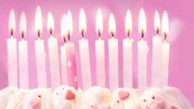 One pink and 12 white birthday candles in birthday cake decorated with pink candy hearts