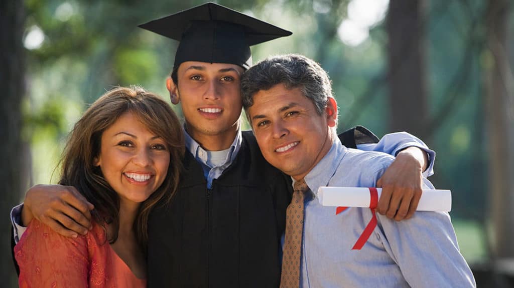 A high school graduate hugging his mom and dad while holding his diploma