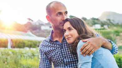 Middle-age couple standing outside. She's leaning against him, he has his arm around her.
