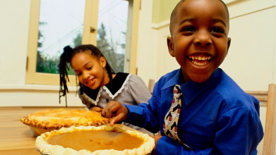 Well-dressed and smiling boy and girl seated at the Thanksgiving dinner table with two pies in front of them
