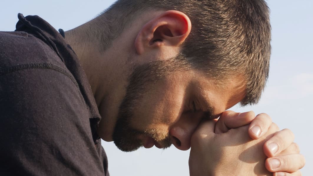 Close-up, profile image of a contrite man with his head bowed, his hands clasped in prayer