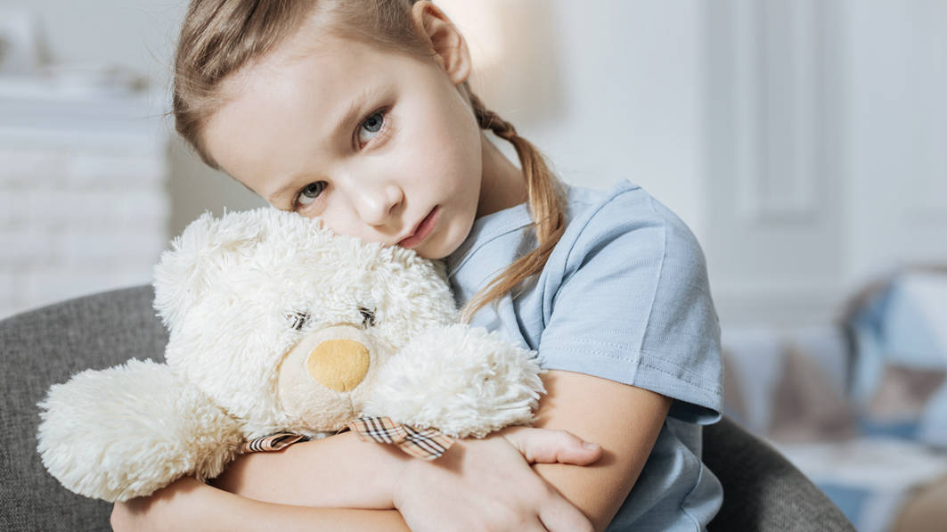 A sad, young girl hugging her teddy bear